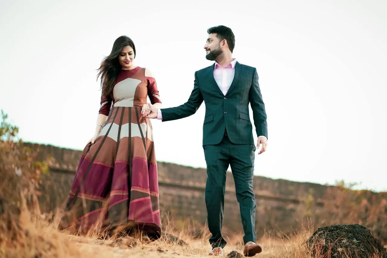 A man and woman holding hands while walking through the grass.